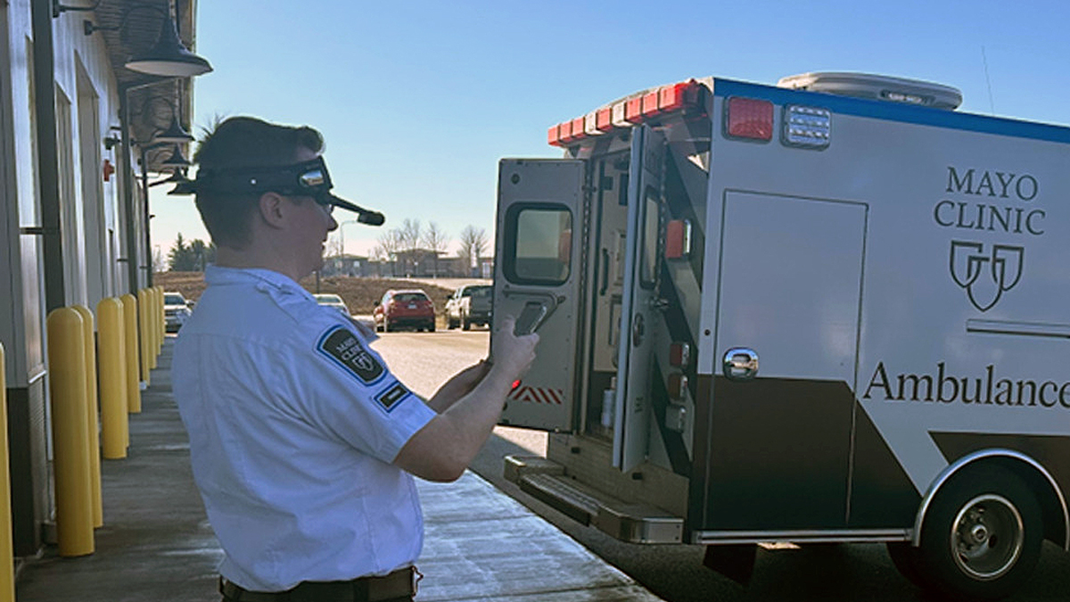 A paramedic wearing OPTAC-X headset near a Mayo Clinic ambulance outside a building.