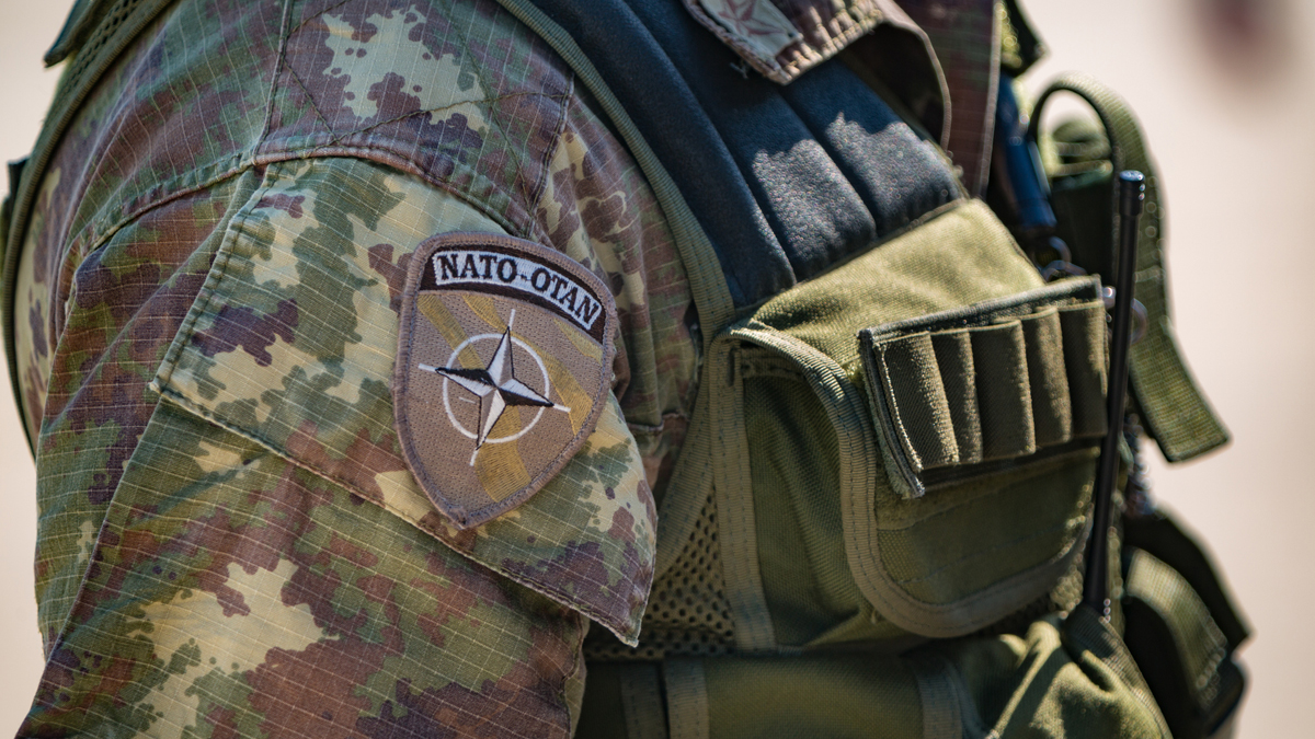 Close-up of a soldier wearing camoflage with a NATO-OTAN patch and tactical gear on the uniform.