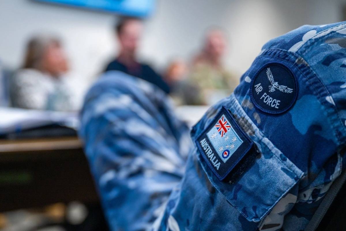 An Australian Air Force uniform sleeve with patches, including one featuring the Australian flag and the words 'Air Force.' The background is blurred, with people in a meeting setting.