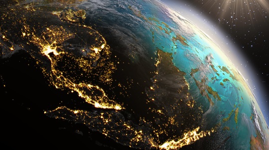 A satellite view of Earth showing Asia and parts of Europe illuminated by city lights at night, with rays of sunlight emerging on the horizon.