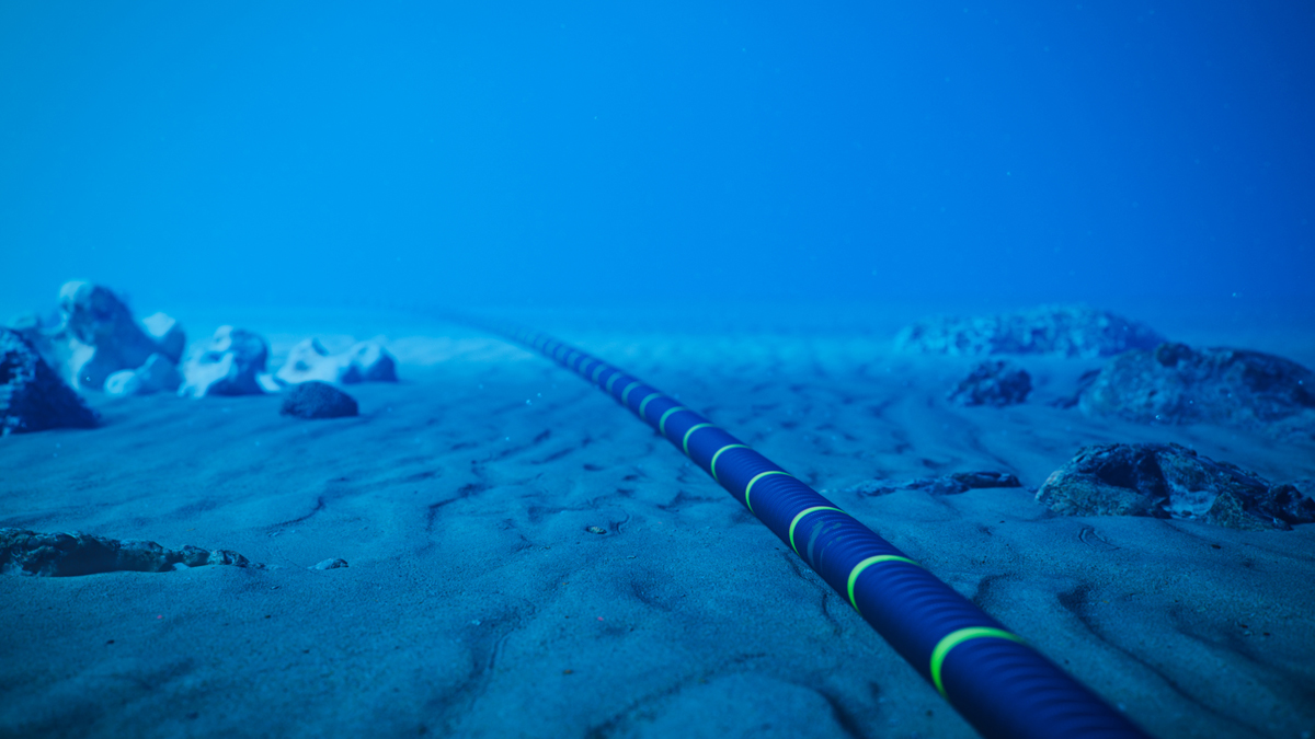 A fiber-optic cable lies on the ocean floor, stretching into the distance under deep blue water.