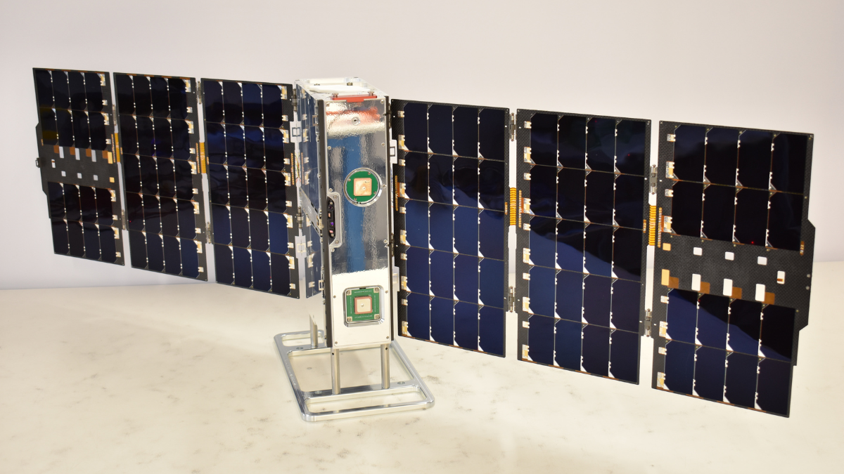 A small satellite with extended solar panels is displayed on a stand.