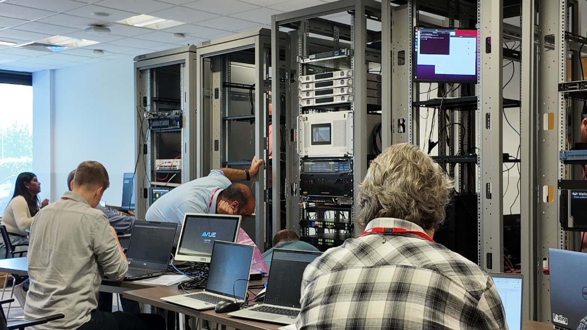 A group of people working on laptops and configuring server racks in a technology lab setting.
