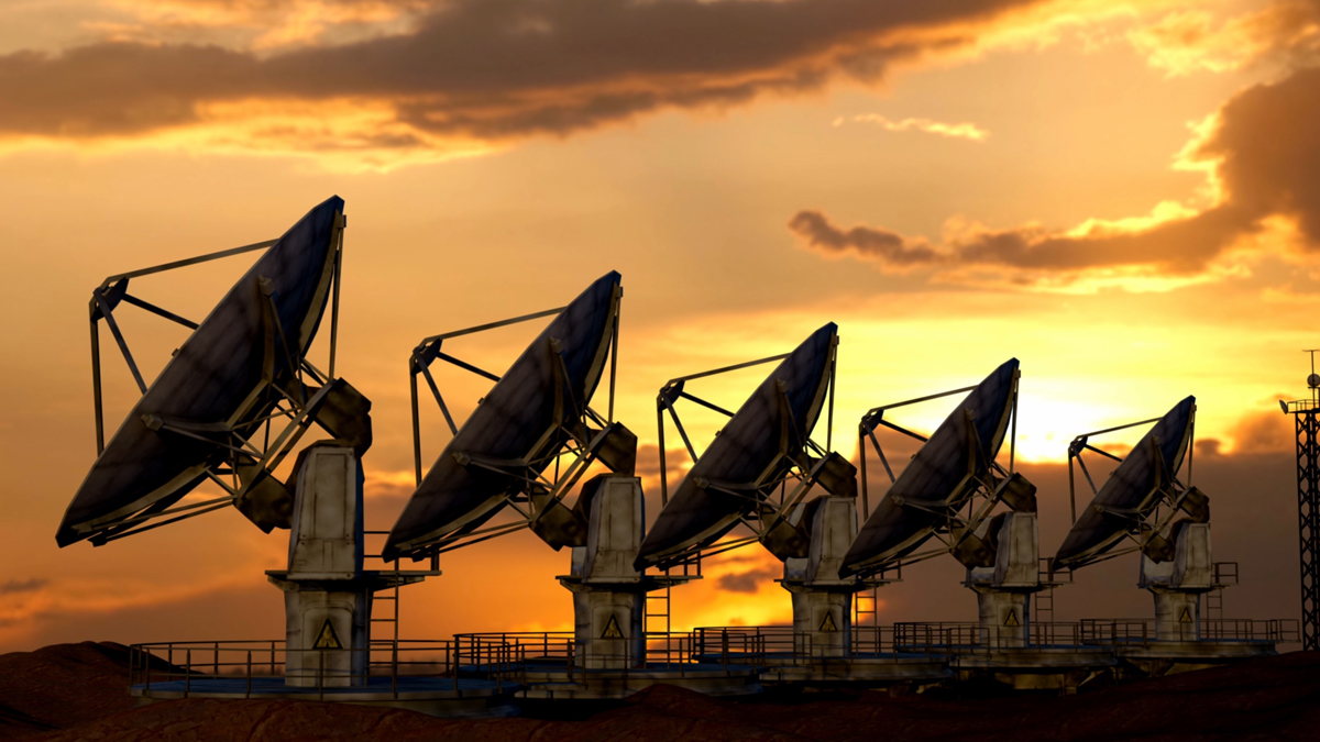 A row of large satellite dishes silhouetted against a dramatic sunset sky.