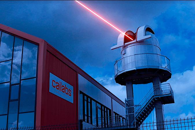 A building with the logo 'Cailabs' and an adjacent structure emitting a red laser beam into the sky.