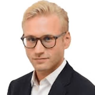 Portrait of a man with blond hair, wearing glasses and a suit, identified as Kacper Grzesiak.