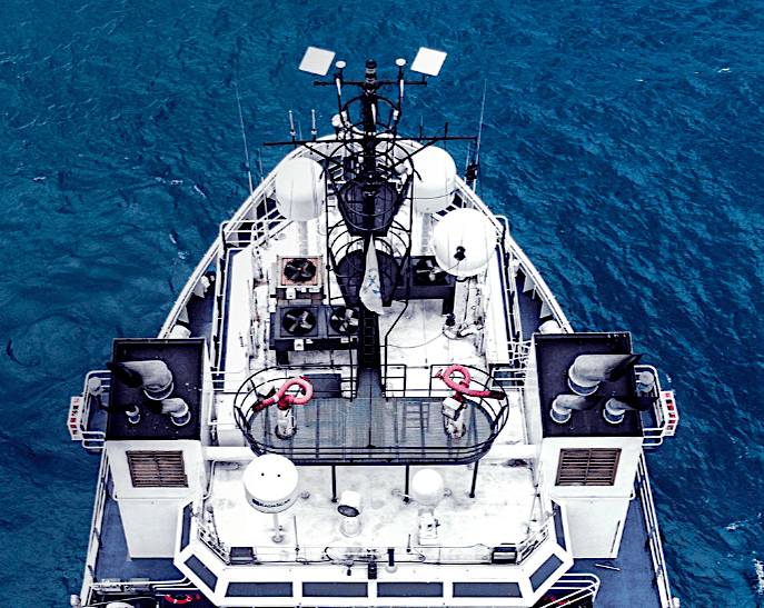 Overhead view of a ship's deck equipped with various antennas and communication equipment, sailing on a blue ocean.