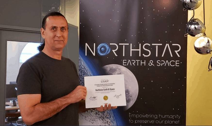 Stewart Bain, Chief Executive of NorthStar Earth & Space, holds an award of recognition in front of a NorthStar Earth & Space banner.