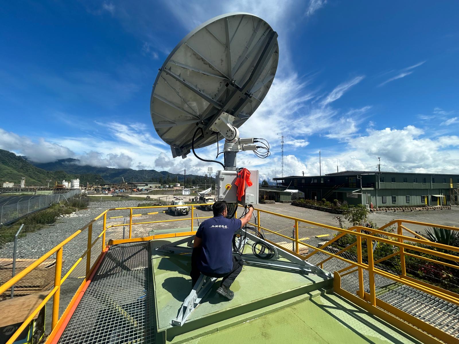 A technician wearing an AXESS shirt configures a multi-orbit satellite terminal on a rooftop platform, supporting mining operations with SES satellite technology.