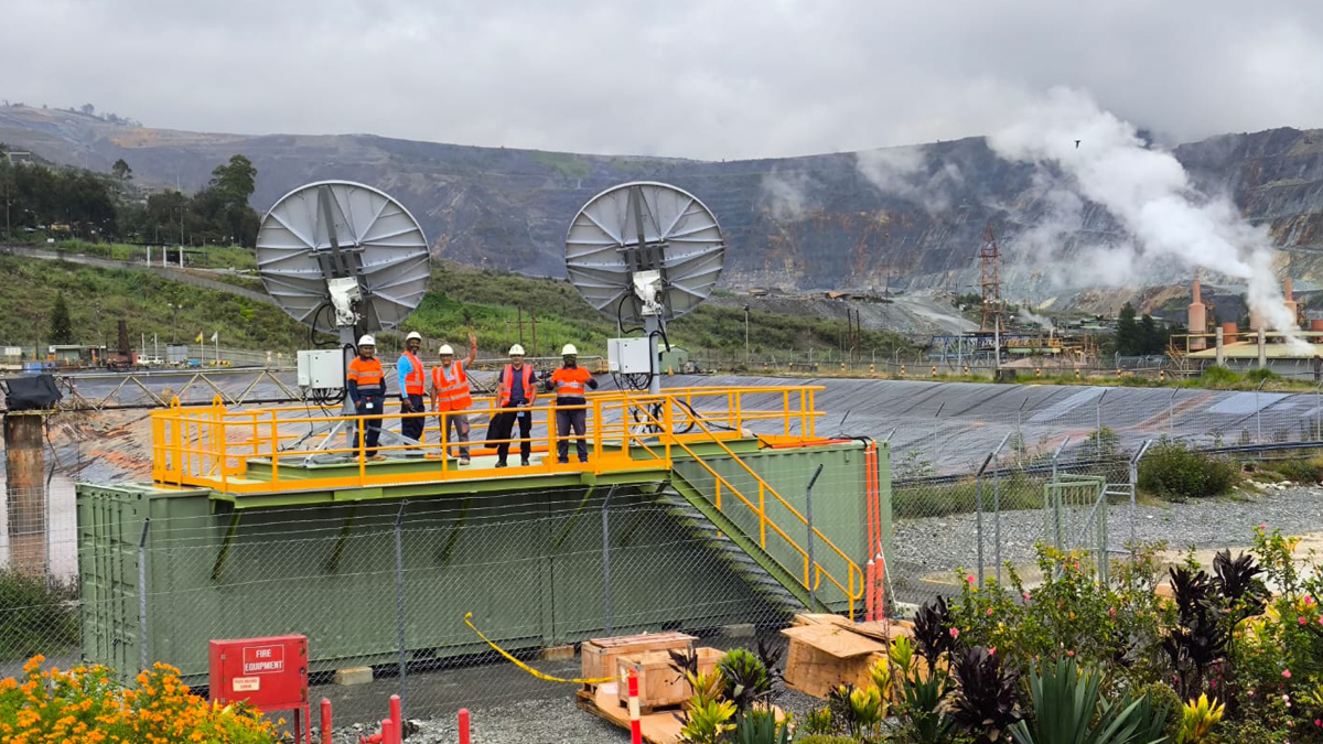 A team of workers stands on a raised platform with two satellite dishes providing SES O3b mPOWER connectivity at a mining site.