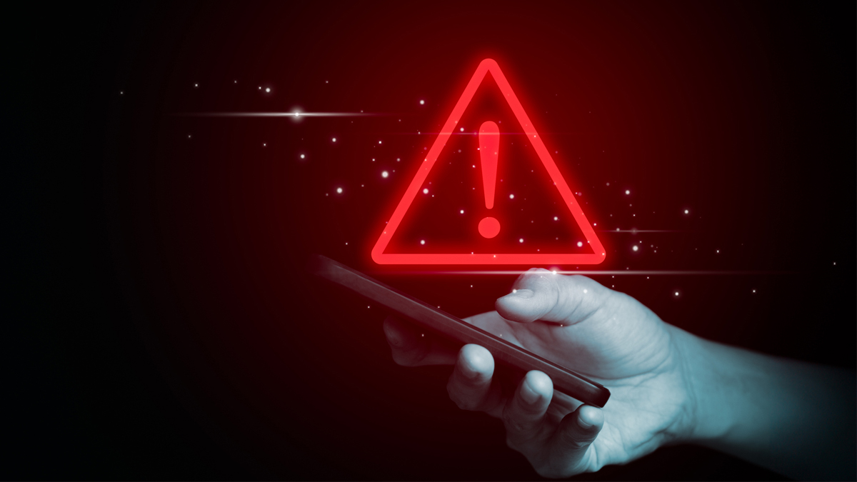  A hand holding a smartphone with a glowing red warning triangle and exclamation mark above it, symbolizing a digital alert or security warning.