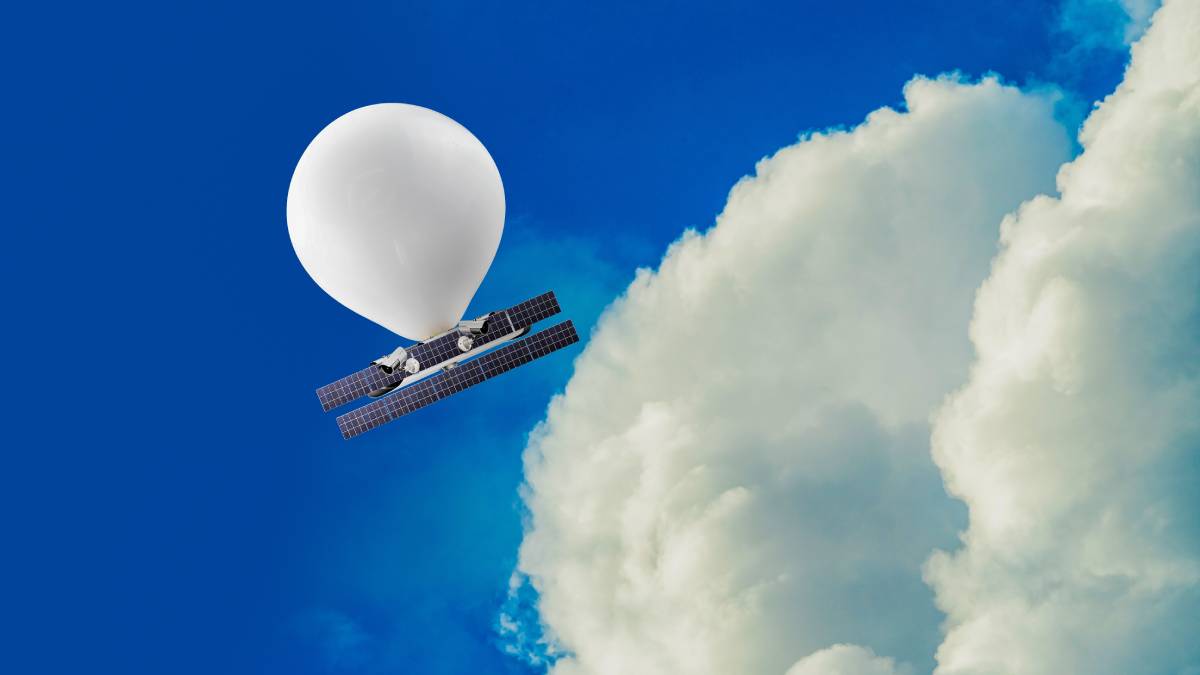 A white high-altitude balloon with solar panels is floating in a blue sky near a large cloud.