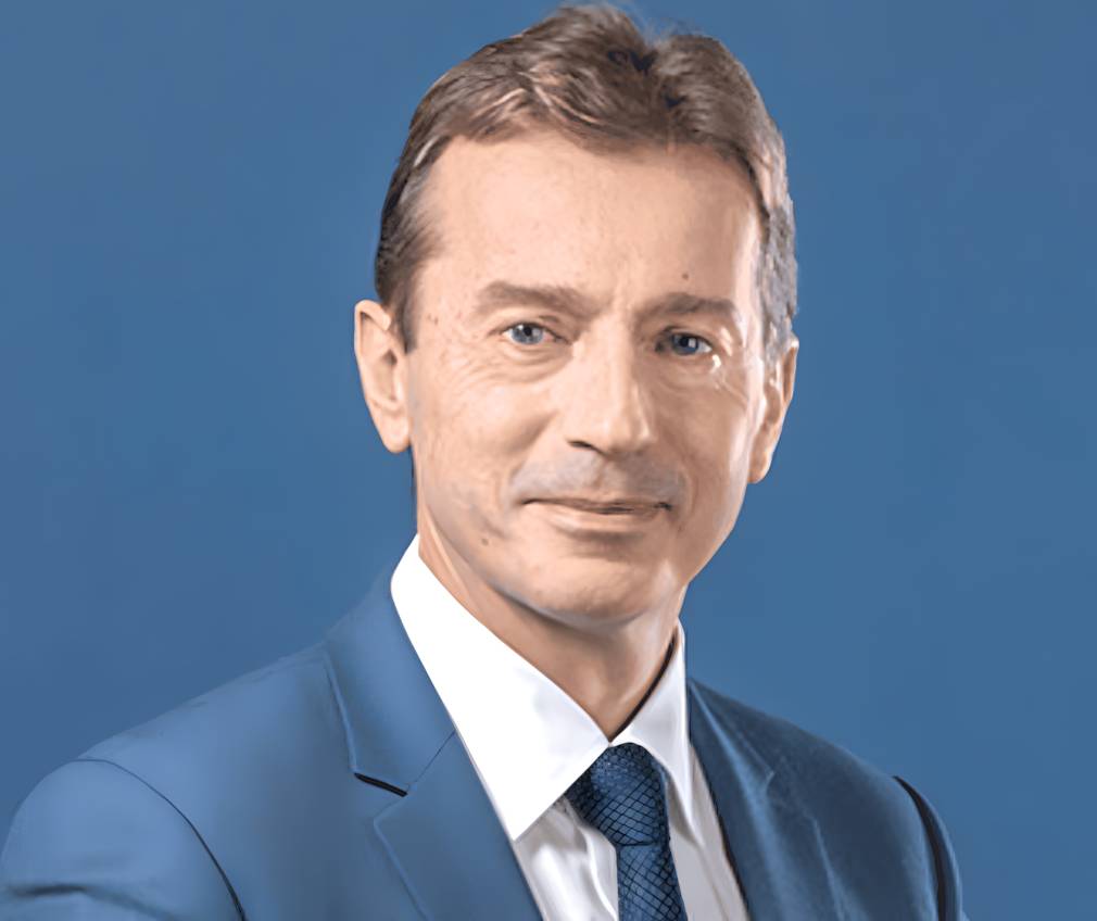 Professional portrait of Guillaume Faury, CEO of Airbus, wearing a blue suit against a solid blue background.