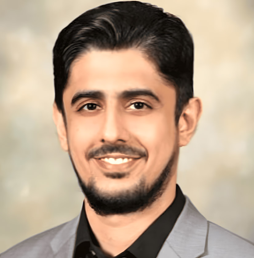 A smiling man with short black hair and a trimmed beard wearing a light gray suit jacket and black shirt, set against a neutral blurred background.