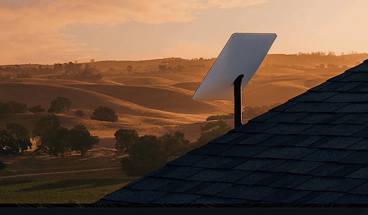 A Starlink satellite dish installed on a rooftop, with a scenic countryside view of rolling hills and trees at sunset.