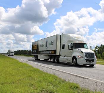 Two white semi-trucks drive in a line on a sunny day, with the lead truck displaying logos for DriveOhio and ODOT, demonstrating Leader Follower Platooning.